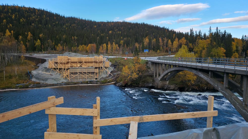 A bridge being built with timber formwork by the river at Stora Blåsjön in Jämtland, Sweden, with autumn forest behind.